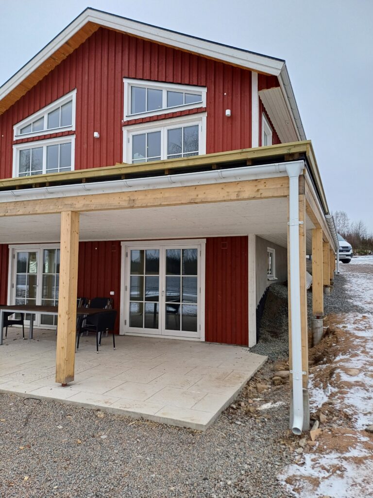 Rött hus med vita fönsterkarmar och stora fönster, en snöig dag.