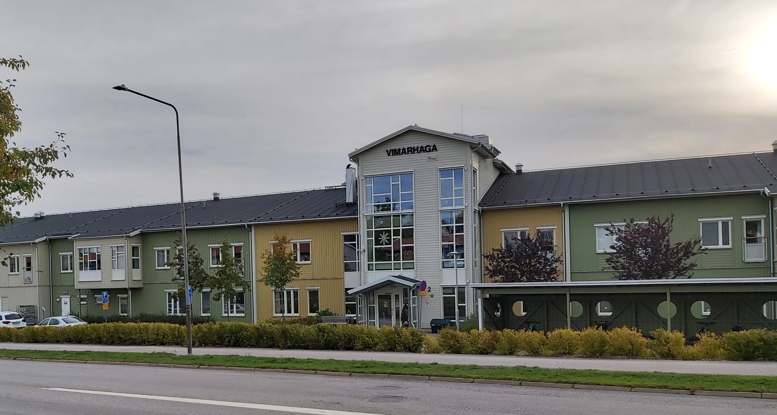 Vimarhaga & Borghaga vård/omsorgsboende Tvåvåningsbyggnad i färgerna beige, gult och grönt, med glasentré och träd framför.
